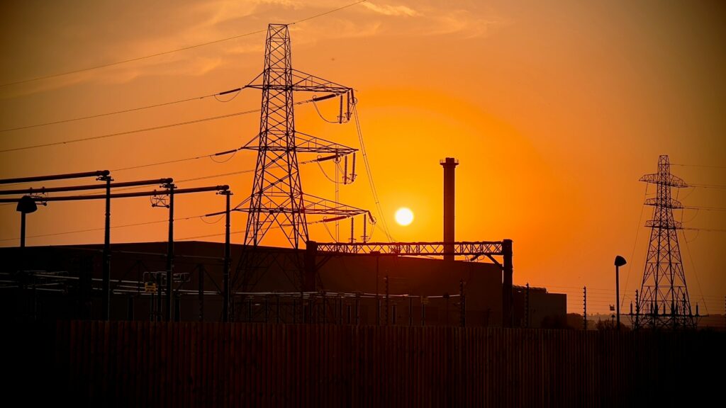Silhouette of power lines and industrial structures against a dramatic sunset.